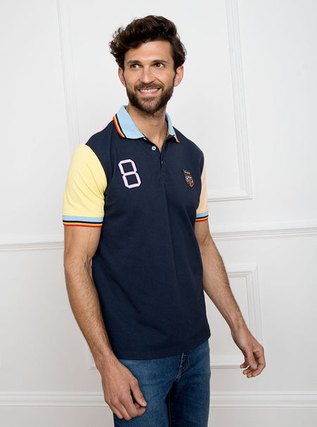 Man wearing navy based multicoloured panelled 100% cotton polo shirt with giant number 8 on pale pink back.